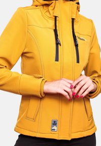 Veste jaune moutarde avec capuche, dotée de fermetures éclair noires, de poignets élastiques et de poches avant ; texture de tissu lisse et durable.