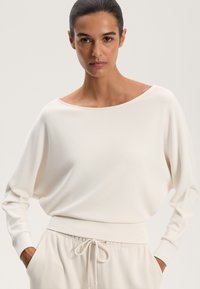 Top ușor, de culoare crem, cu decolteu larg în stil barcă și o siluetă relaxată. Are mâneci lungi și o textură moale pentru confort.