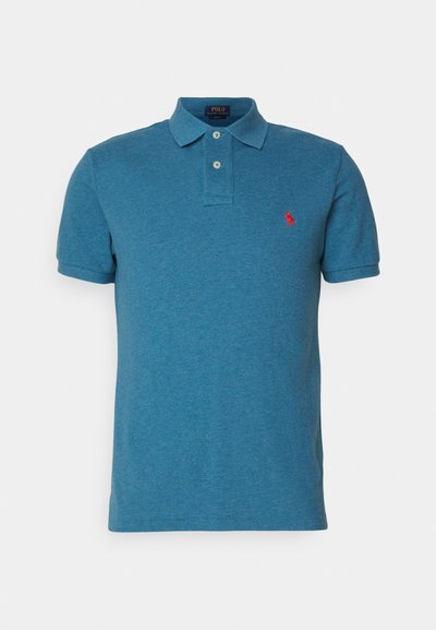 Sinaise maheline polo särk, millel on volditud krae, kahe nupuga läbilõige, lühikesed varrukad ja väike punane logo vasakul rinnal. Silmadega pehme tekstuur.
