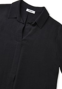 Camicia nera con colletto, dotata di una chiusura a bottoni frontale, realizzata in tessuto testurizzato, caratterizzata da una vestibilità comoda e orlo dritto. Etichetta del marchio visibile.