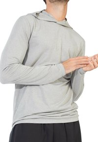 Lichtgrijze longsleeve pullover van een gestructureerde ribstof, met een capuchon en aansluitende mouwen, gecombineerd met donkere broeken.