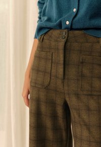 Braun karierte Hosen mit einer sanften Textur, ausgestattet mit zwei Gesäßtaschen und zwei Knöpfen am Bund, kombiniert mit einem blauen Strickoberteil.