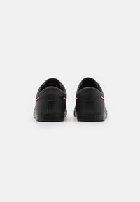 Schwarze Ledersneaker mit einer glatten Textur, die eine kontrastierende rote Akzentlinie entlang der Seite und eine Gummisohle aufweisen.