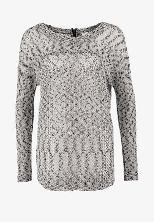 Femme portant un pull en maille gris, un pantalon en cuir noir, des bottes noires, tenant un grand sac fourre-tout en cuir noir.