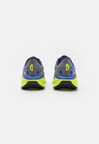 Baskets de course avec une tige en mesh gris, des accents bleus et une semelle jaune vif. Présentent une surface texturée et un détail de logo distinct.