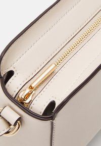 Interior de bolso de cuero beige con cremallera dorada, forro crema y ribete marrón. Los detalles de la cremallera son prominentes, proporcionando un cierre seguro.