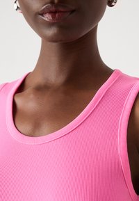 Tettsydd rosa ribbet tanktop med scoop-hals, som viser en jevn tekstur og definerte sømdetaljer langs kantene.