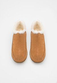 Chaussons en suède beige avec une doublure blanche duveteuse, ornés de coutures décoratives le long des bords et d'une semelle plate et texturée.