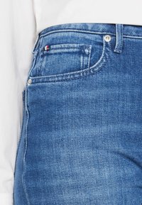 Denimjeans i medelblått med en klassisk passform. Har en framficka, silverfärgad hårdvara och en liten detalj med röd, vit och blå logotyp.