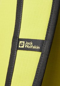 Fel geel stof met een gestructureerd oppervlak, omrand door zwarte stiksel. Heeft een klein Jack Wolfskin-logo in een rechthoek.