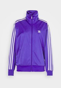 Lila zip-up jacka i glänsande tyg, med hög krage, vit tre-stripes design på ärmarna och en liten vit logotyp på bröstet.