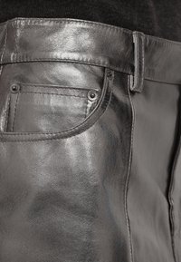 Gros plan sur un pantalon en cuir noir brillant montrant une poche avant, une boucle de ceinture et une surface en cuir texturée.