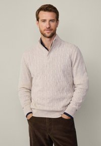 Cremefarbener Kabelstrickpullover mit hohem Kragen, gerippten Bündchen und Saum. Enthält einen marineblauen Akzent am inneren Rand des Kragens. Lässiges Design.