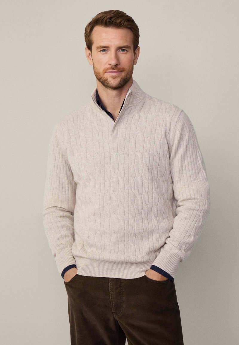 Cremefarbener Kabelstrickpullover mit hohem Kragen, gerippten Bündchen und Saum. Enthält einen marineblauen Akzent am inneren Rand des Kragens. Lässiges Design.