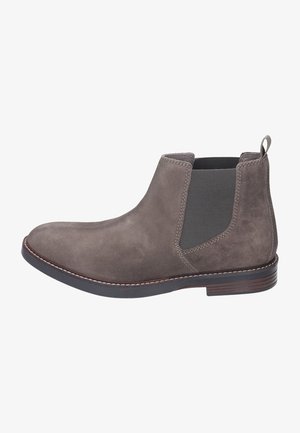 Šedá nubuková kotníková bota s elastickými bočními panely, poutkem pro snadné nazouvání a plochou gumovou podrážkou. Disponuje prošívaným okrajem a zaobleným designem špičky.