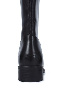 Black leather boot with stacked heel and visible stitching, shown from the back on a white background.