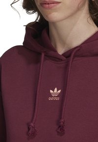 Marin hoodie med snörning och tofsar, med en subtil ljusrosa Adidas-logotyp på bröstet, tillverkad av mjukt, strukturerat tyg.