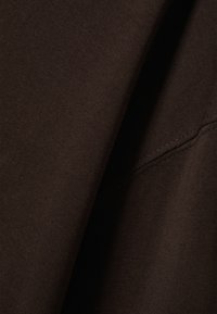 Tmavě hnědá látka s hladkou strukturou a jemným žebrováním. Viditelné švy podél okraje dodávají designu na detailu.