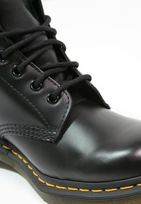 Svart läder ankle boot med rund tå, texturerad yta, svarta snören och gula sömmar längs sulan. Har silverfärgade öglor.