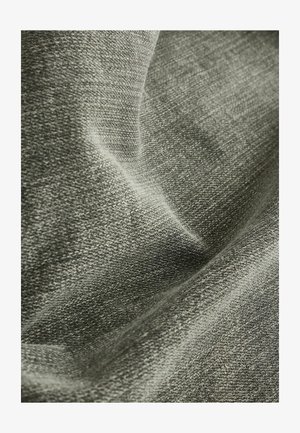 Lähivõte pehmest, tekstuurses hallist kangast, millel on nähtav kudumismuster ja õrnad voldid, mis loovad varje ja helendusi.