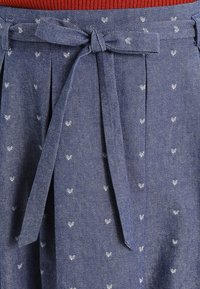 Džínová sukně s modrým základem a malými bílými srdíčky, s vázacím pasem a plisovaným designem. Hladká textura.