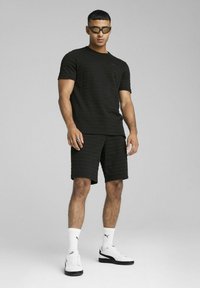 Sort stribet kortærmet skjorte parret med matchende shorts. Hvide sneakers med sorte detaljer og hvide sokker. Simpel, atletisk design.