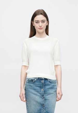 Weißer, kurzärmeliger Strickpullover mit Rippstruktur und Rundhalsausschnitt, kombiniert mit einem blauen Denim-Rock mit vorderer Knopfleiste.