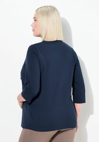 Marineblaue Dreiviertelarmbluse aus weichem Stoff. Sie hat einen Rundhalsausschnitt und einen lockeren Schnitt mit abgerundetem Saum.