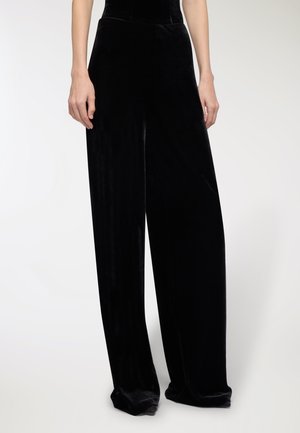 Pantaloni ampi in velluto nero con una texture liscia, caratterizzati da una vita alta e un design lungo e fluente. Mettono in risalto una silhouette rilassata.