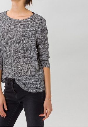 Halenka s dlouhým rukávem v černobílé leopardí potisku, s kulatým výstřihem a volným střihem, doplněná černými džíny.