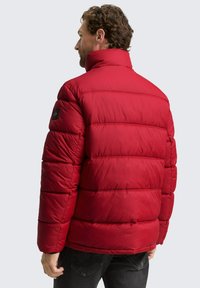 Crvena jakna s punjenjem, visoki ovratnik, horizontalne šavove i oznaku na lijevom rukavu. Glatka tekstura, topli dizajn i robusni izgled.