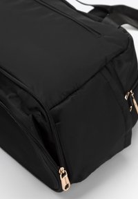 Sac à dos noir au design épuré, fabriqué en matériau doux et durable. Comprend des fermetures éclair visibles et des accents en quincaillerie dorée.