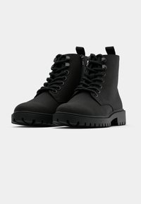 Botas negras hasta el tobillo con acabado mate, punta redonda, suela de goma gruesa, cordones en la parte delantera y cierre de cremallera lateral para un fácil uso.