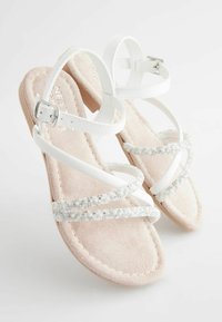 Sandali bianchi con cinghie sottili, caratterizzati da un accentuato perla scintillante, un plantare in morbida suede rosa e una leggera suola in legno. Fibbia regolabile alla caviglia.