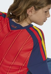 Röd och marinblå fotbollströja med gula ränder, med en strukturerad design och "España" sydd vid bakre halsen.