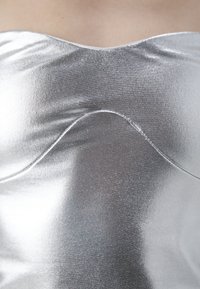 Metallisk silverfärgad strapless topp med en slät, glansig textur. Har en böjd söm över bröstområdet för formning.