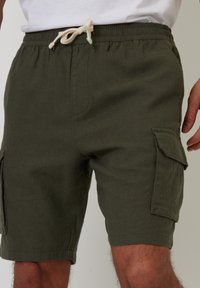 Grüne Cargo-Shorts aus strukturiertem Stoff, ausgestattet mit einem elastischen Bund und Kordelzug sowie seitlichen Taschen für praktische Nutzung.