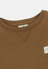 Pull en maille marron à col rond avec col côtelé et une petite étiquette rectangulaire blanche sur la poitrine.