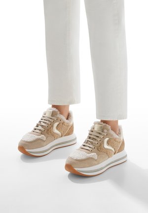 Beige sneakers with a plush texture, suede and furry accents, thick white midsole, and rubber outsole. Lace-up design with gold hardware.