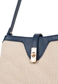 Borsa a tracolla in tessuto beige testurizzato con dettagli in pelle blu navy, caratterizzata da una chiusura dorata e una singola tracolla regolabile.