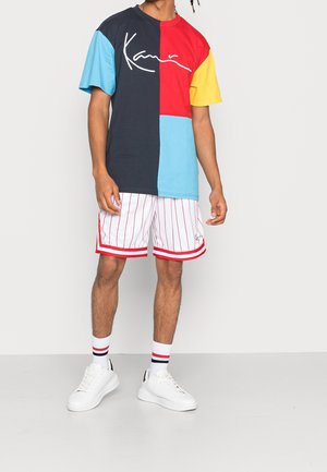 Heren T-shirt met kleurvakken in marineblauw, rood, geel en lichtblauw, met witte, geschreven tekst. Gecombineerd met witte gestreepte shorts.
