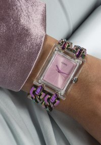 Montre rectangulaire transparente avec un cadran rose, des aiguilles violettes et un bracelet en maillons multicolores. Des accents métalliques lisses améliorent le design.
