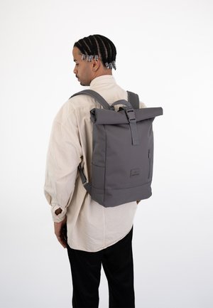 Roll-top gray backpack made of sturdy material, featuring adjustable straps, a front zip pocket, and a logo patch on the side.