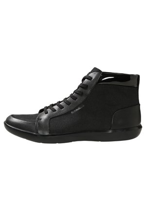 Mustat korkeavartiset lenkkitossut, joissa kangasta ja nahkaa, nauhallinen edusta ja tasainen kumipohja, nähtynä sisäpuolelta.