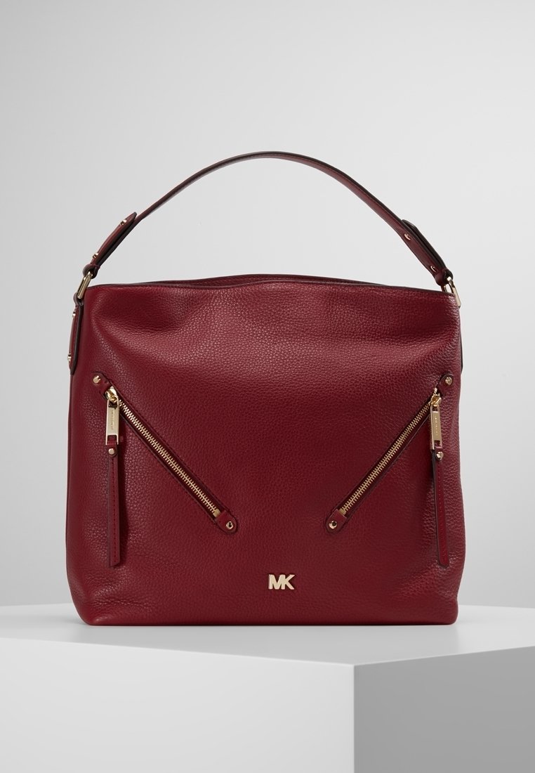 Sac à main en cuir rouge foncé avec deux poches zippées en diagonale à l'avant et une seule poignée, avec le logo doré MK en bas au centre.