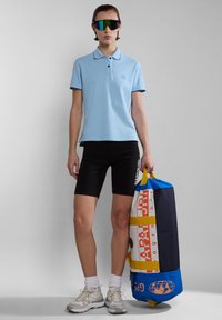 Světle modré polo tričko s tmavým lemem, černé cyklistické kraťasy a barevná sportovní taška. Model má na sobě reflexní sluneční brýle a tenisky.