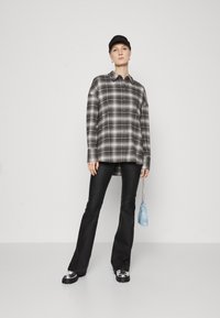 Camicia a quadri nera e bianca oversize con maniche lunghe, abbinata a pantaloni neri a zampa d'elefante e sneaker chunky. Piccola borsa blu con catena.