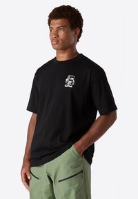 Black short-sleeve t-shirt made of cotton, featuring a small white graphic design on the left chest area. Worn with green cargo shorts.