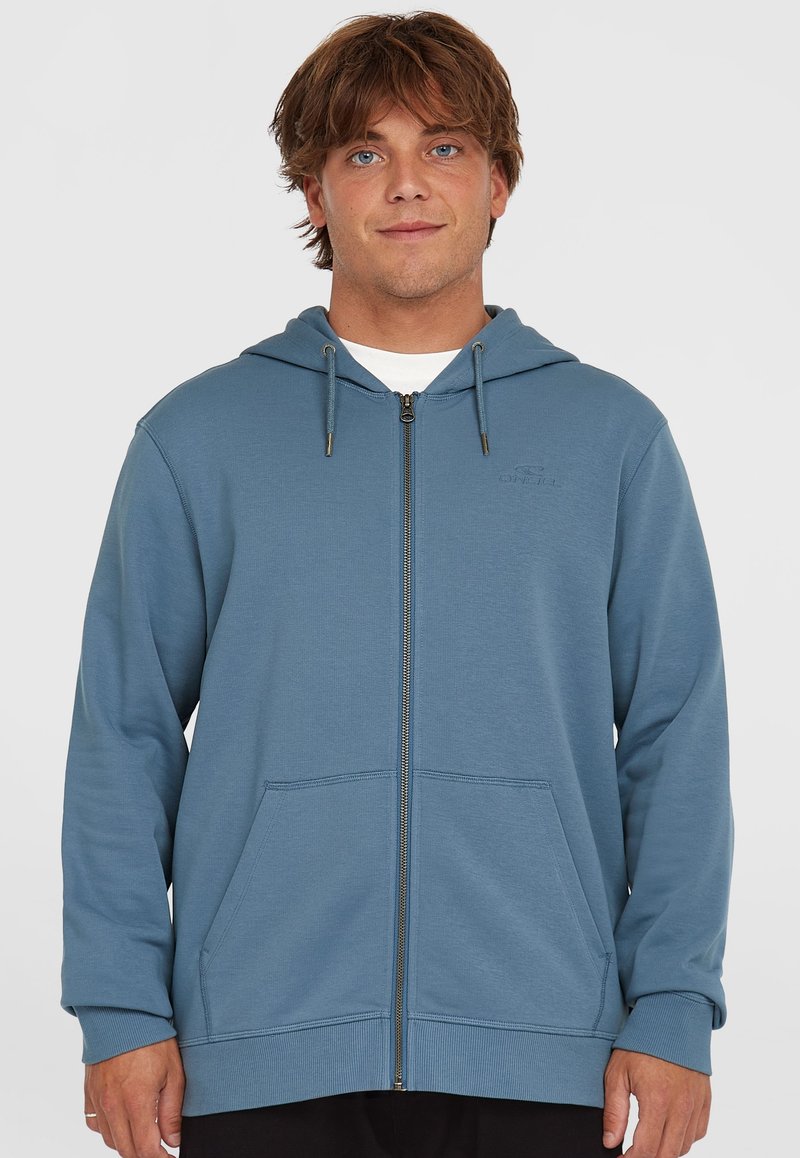 Blue zip-up hoodie made of soft fabric, featuring a hood, two front pockets, and a small logo on the left chest. Smooth texture.