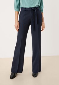 Marineblauwe op maat gemaakte broek met een wide-leg ontwerp, een riem in de taille en een gladde stoftextuur. Gecombineerd met een lichtgroene top en zwarte enkellaarsjes.